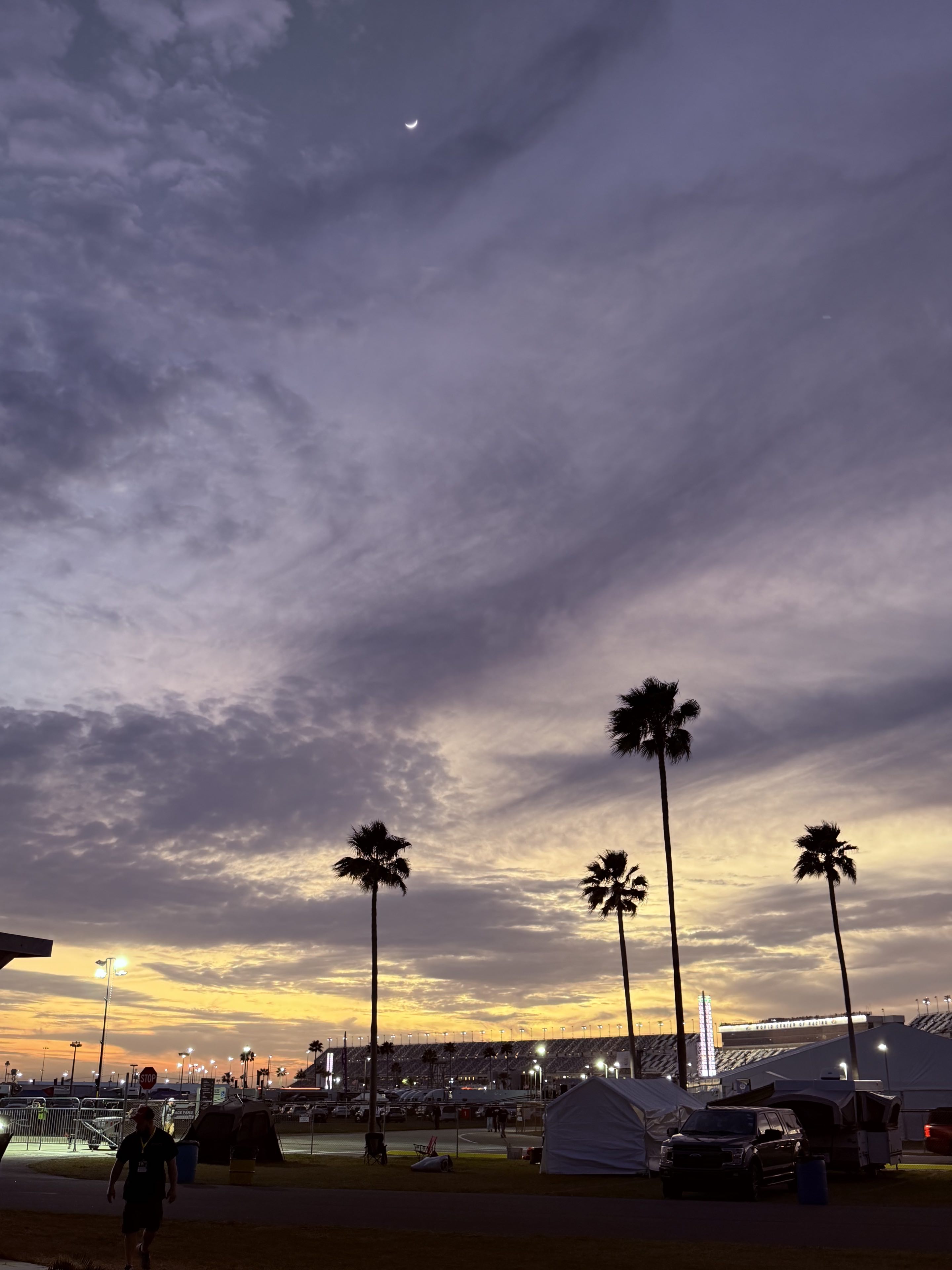 The sky above the infield of Daytona International Speedway at dusk with the waxing crescent moon above